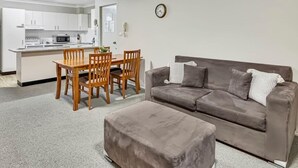 A compact living space with a kitchenette, a dining area, and a seating area with a sofa and ottoman. - Glenmore Lodge - CBD Location, Hidden Gem (Dubbo)