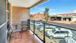 A balcony with a brick wall, a small table with chairs, and a view of police cars on the street. - Glenmore Lodge - CBD Location, Hidden Gem (Dubbo)