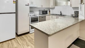 A modern kitchen with white cabinetry, a granite countertop, and stainless steel appliances including a refrigerator, microwave, and oven. - Glenmore Lodge - CBD Location, Hidden Gem (Dubbo)