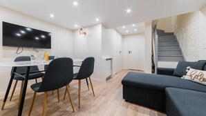 A modern living room with a flat-screen TV, a dining area with chairs and a table, a sofa with a 'hello' pillow, and a staircase. - Sous Plex palais des congres Porte Maillot - 4P (Neuilly-sur-Seine)