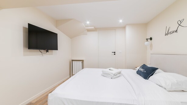 A bedroom with a bed, a flat-screen TV mounted on the wall, a door, and a wall-mounted light fixture. - Sous Plex palais des congres Porte Maillot - 4P (Neuilly-sur-Seine)