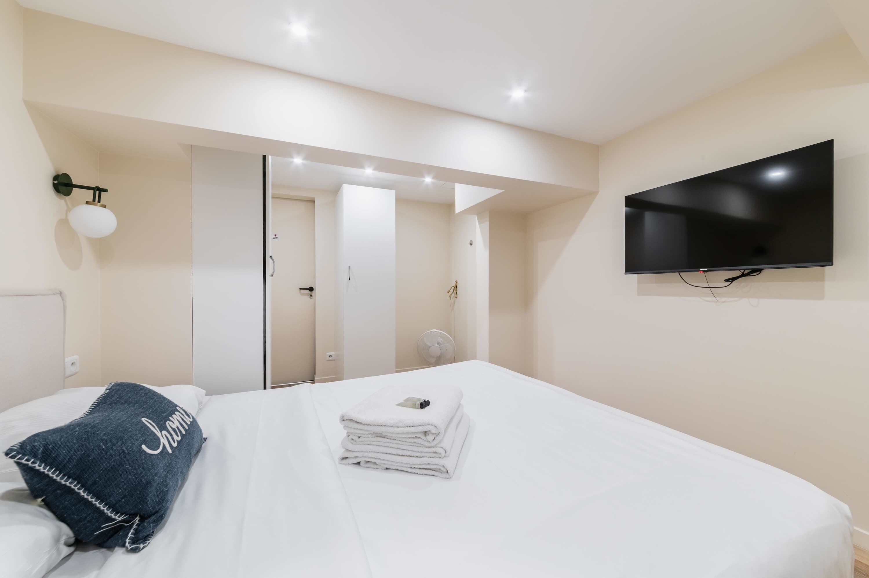 Habitación de hotel con cama, televisión, espejo y lámpara de pared.