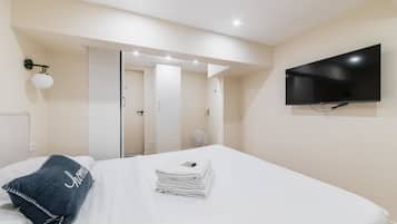 A hotel room with a bed, a television, a mirror, and a wall-mounted light fixture.