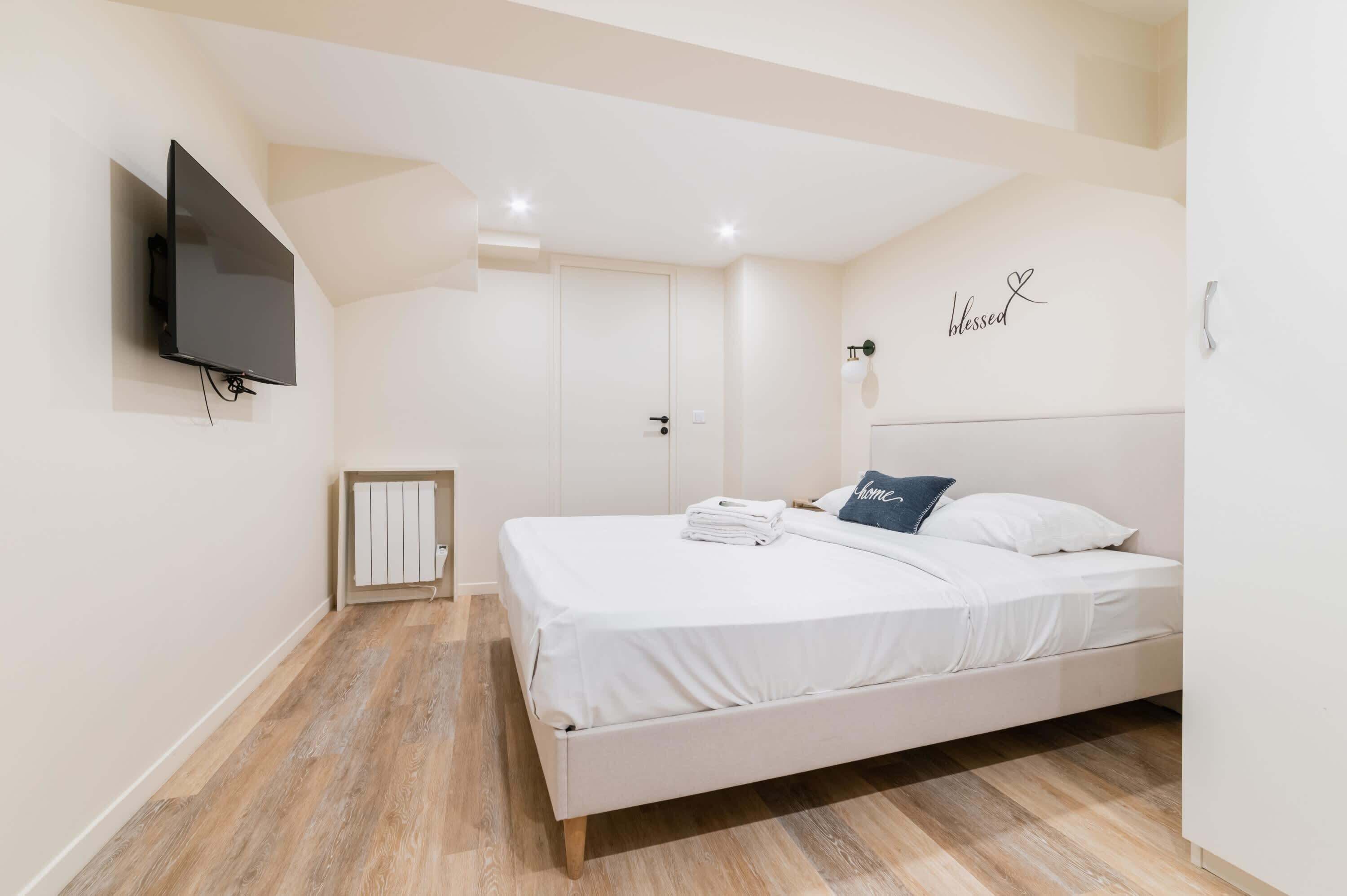 A bedroom with a bed, a wall-mounted TV, a radiator, and a door.
