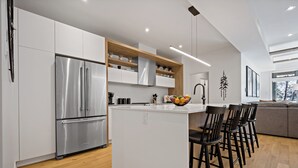 Una cocina moderna con armarios blancos, un refrigerador de acero inoxidable, estantes de madera y una isla central con taburetes de bar.