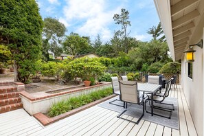 Enjoy dining or socializing on the patio with a table and chairs, surrounded by lush greenery and a brick border.
