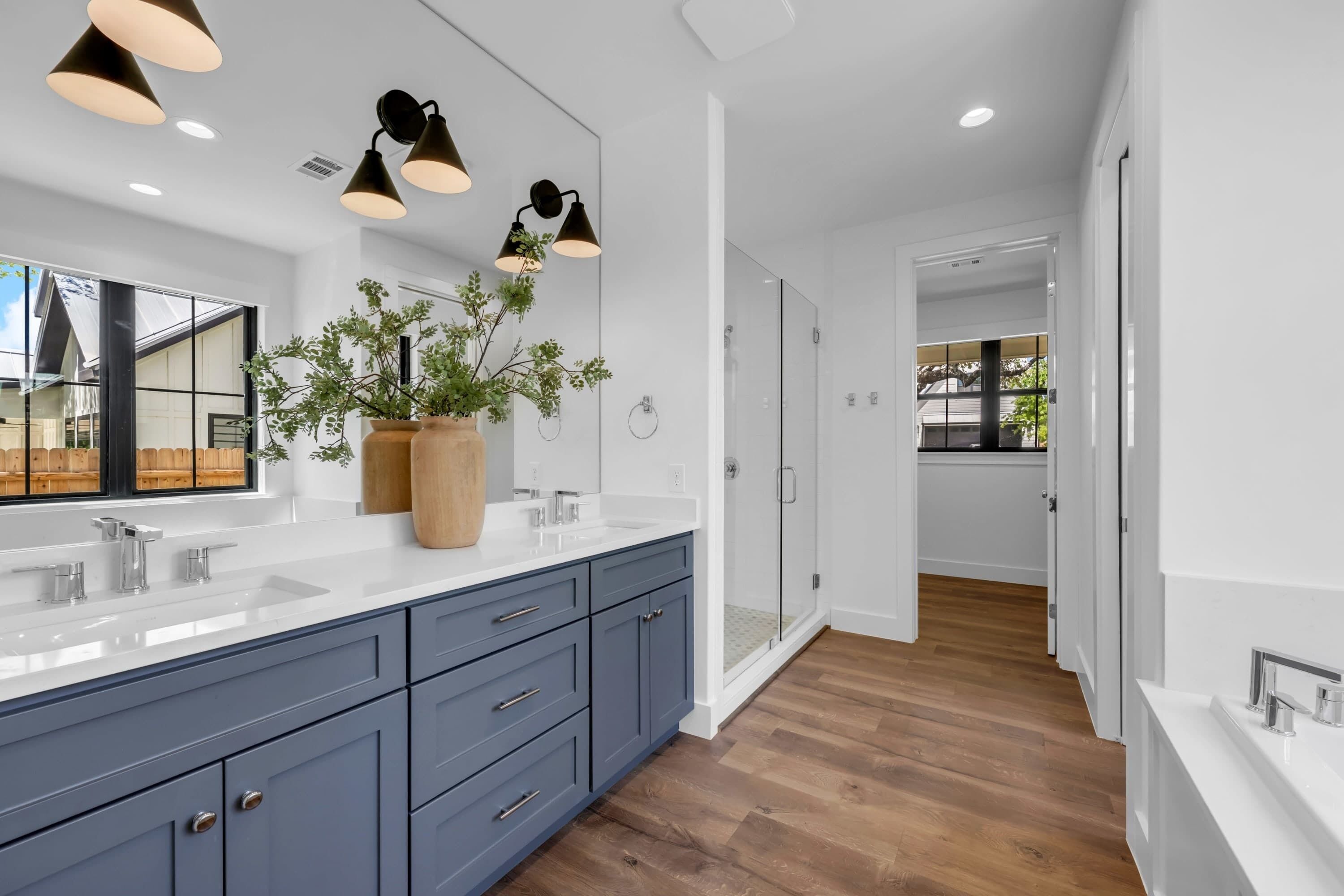 A modern bathroom with dual sinks, a large mirror, and a potted plant.