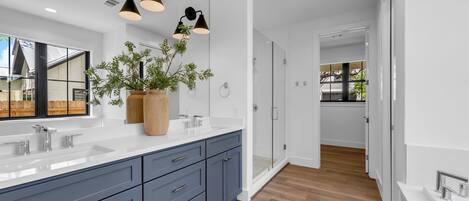A modern bathroom with dual sinks, a large mirror, and a potted plant.