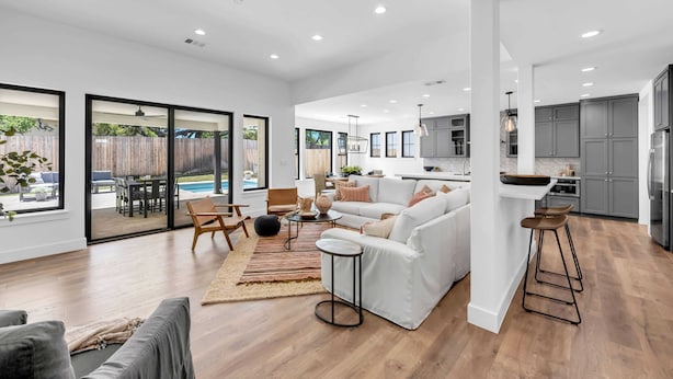 A spacious living area with a large sofa, a coffee table, and a dining table. There is a kitchen area with modern appliances and a bar stool. - Butterfly:  Luxury w/pool, boat slip, sports court (Kingsland)
