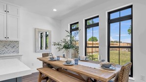 A modern kitchen with a wooden table set for four, large windows, and a view of the outdoors. - Dragonfly: Luxury w/pool, boat slip, sports court (Kingsland)