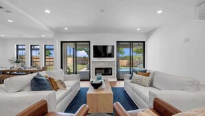 A modern living room with a fireplace, a flat-screen TV, and a dining area with a wooden table and chairs. - Dragonfly: Luxury w/pool, boat slip, sports court (Kingsland)