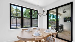 A dining area with a round wooden table set for four, large windows, and a view of the backyard. - Firefly: Luxury w/pool, boat slip, sports court (Kingsland)