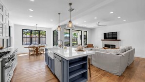 A modern kitchen with a central island, wooden flooring, and a dining area with a table and chairs. - Firefly: Luxury w/pool, boat slip, sports court (Kingsland)