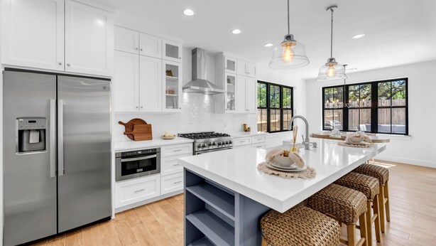 A modern kitchen with white cabinetry, stainless steel appliances, a large island with bar stools, and pendant lighting. - Firefly: Luxury w/pool, boat slip, sports court (Kingsland)