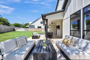 A modern outdoor patio with a white sofa, a black table, and a ceiling fan.