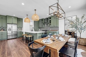A modern kitchen with green cabinets, a stainless steel refrigerator, and a wooden dining table set for six.
