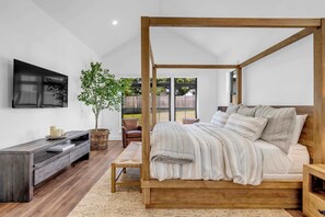 A modern bedroom with a four-poster bed, a flat-screen TV, a wooden bench, and a large potted plant.