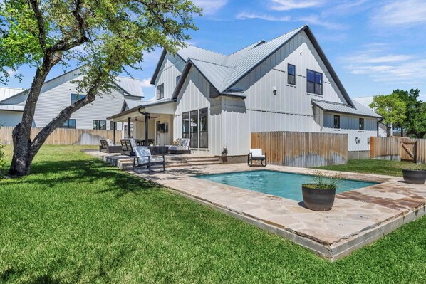 A modern house with a swimming pool, a covered patio, and a fenced backyard.
