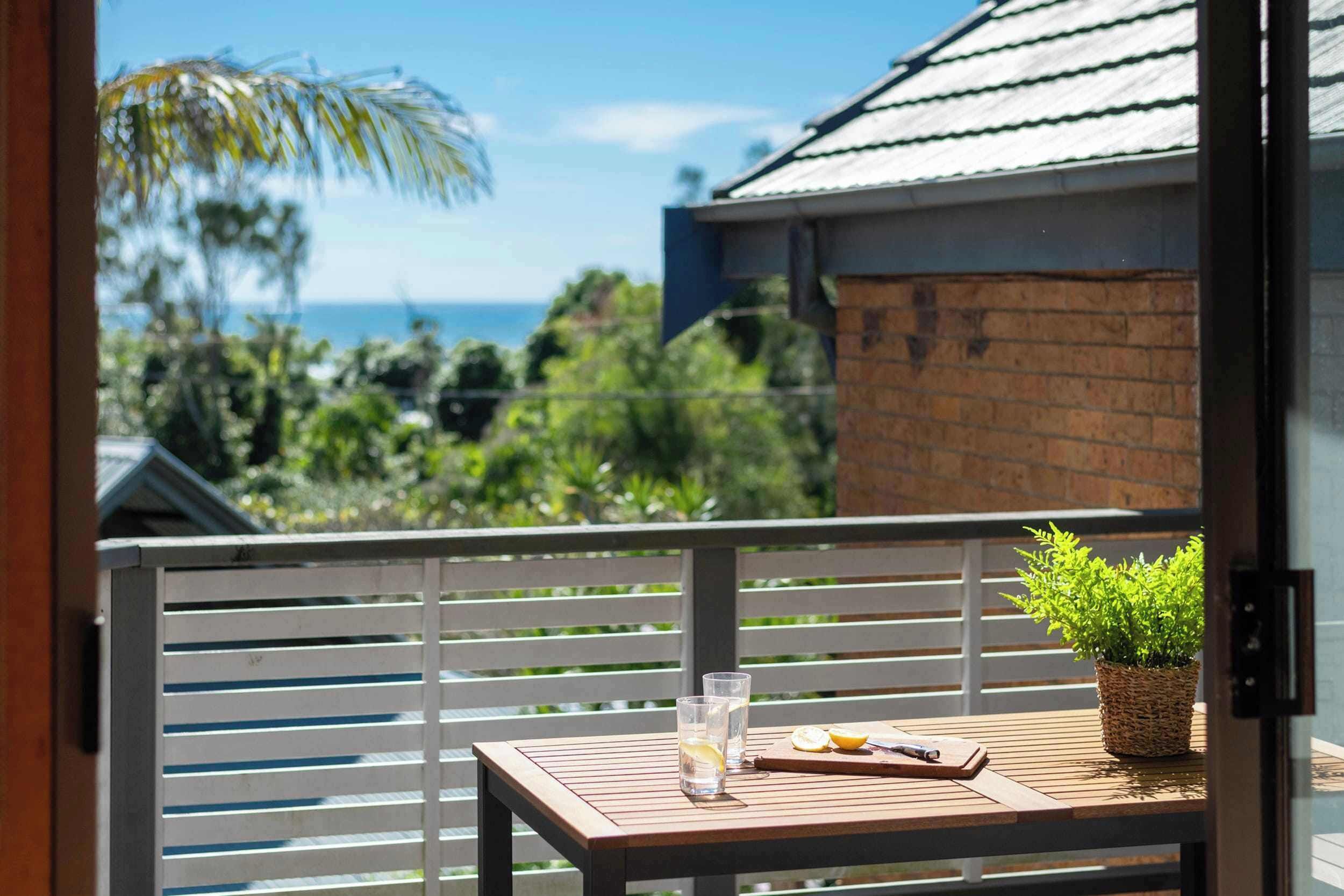 A balcony with a table, two glasses, a plant, and a view of the ocean.