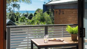 A balcony with a table, two glasses, a plant, and a view of the ocean. - The Surf Pad - Oceanstays - Pet Friendly (Angourie)