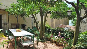 Un patio con mesa y sillas, rodeado de plantas en macetas y un techo de tejas.