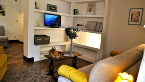 Una sala de estar con televisor, estantes con diversos objetos, una mesa de centro y un sofá.