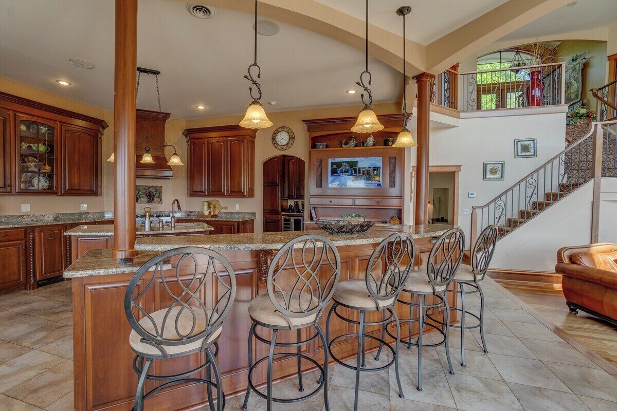 A spacious kitchen with a large island, bar stools, and a staircase leading to an upper level.