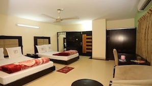 Quarto de hotel com duas camas, um ventilador de teto, uma mesa com cadeira e uma janela com cortinas.