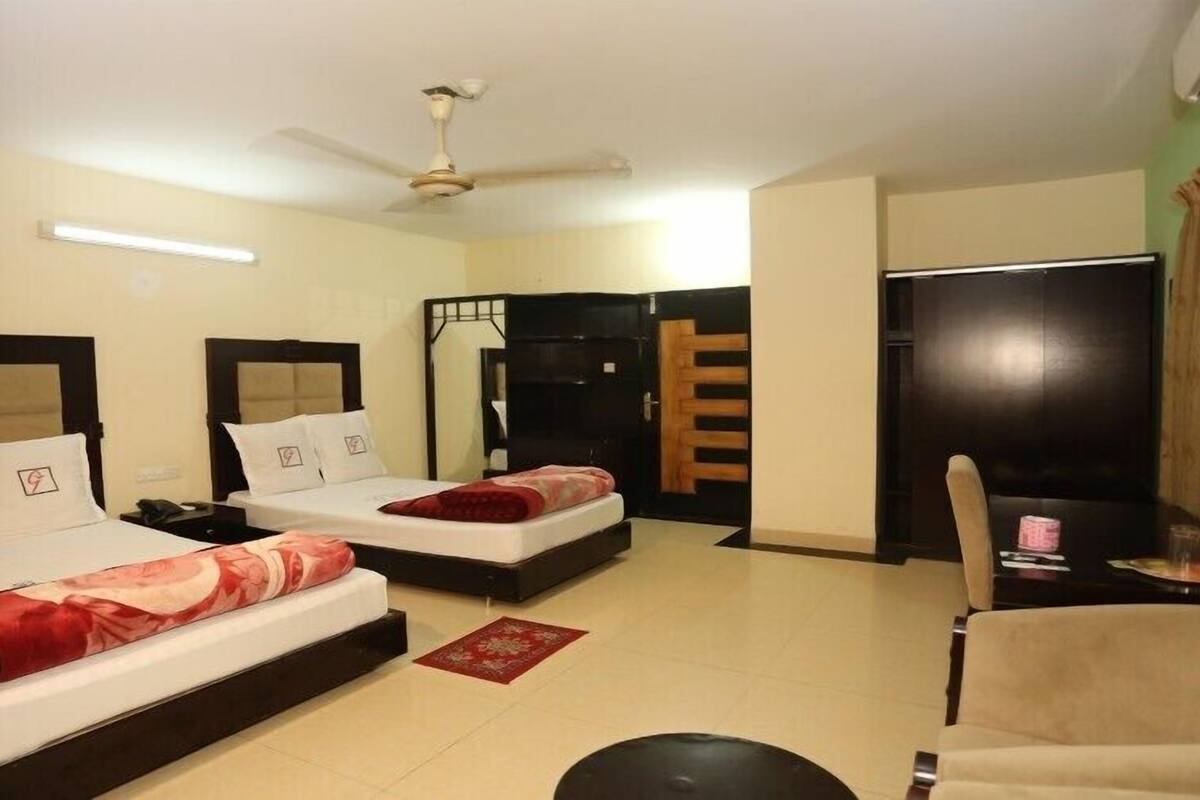 A hotel room with two beds, a ceiling fan, a desk with a chair, and a window with curtains.