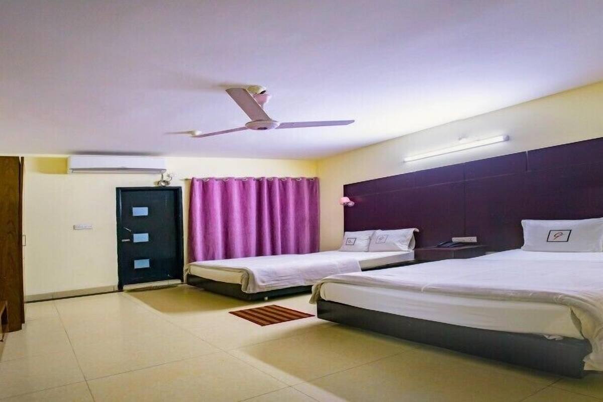 A hotel room with two single beds, a ceiling fan, a dark headboard, and a door with a purple curtain.