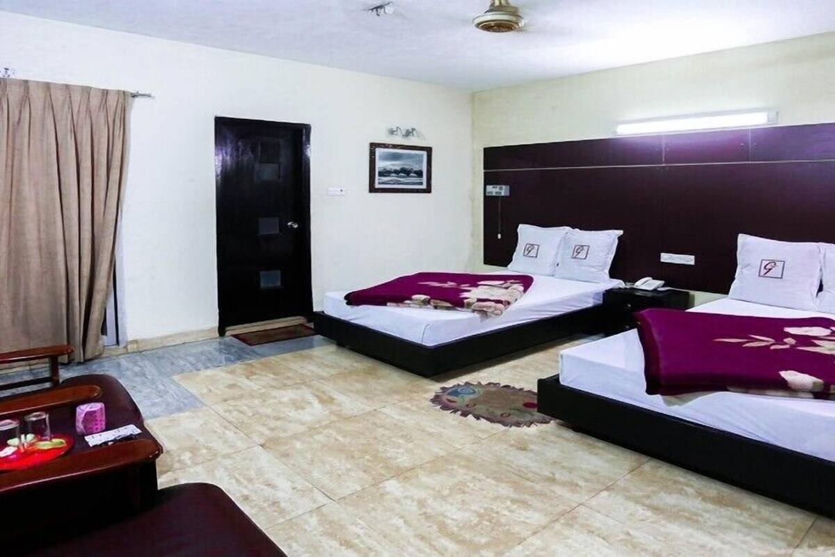 A hotel room with two beds, a desk with a chair, a door, and a window with curtains.