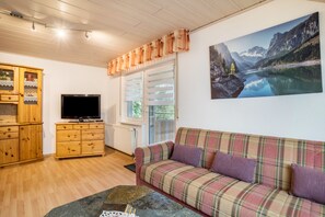 Un salon avec un canapé à carreaux, des meubles en bois, un téléviseur à écran plat et un grand tableau représentant un paysage.
