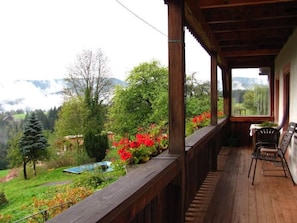 Un balcon en bois offrant une vue sur un paysage montagneux, une petite piscine et une table avec des chaises.