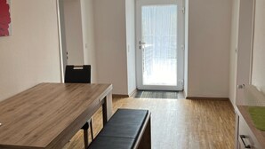 Une pièce avec une table à manger en bois, un banc et, vue par une porte, un balcon.