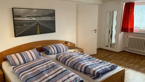 Une chambre à coucher avec un lit, une porte, une fenêtre avec des rideaux, un radiateur et un tableau accroché au mur.