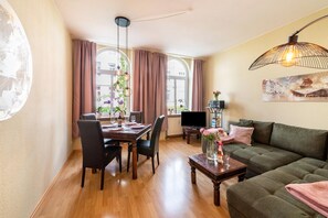 A modern living room with a dining area, a sofa, a TV, and a large window with curtains.