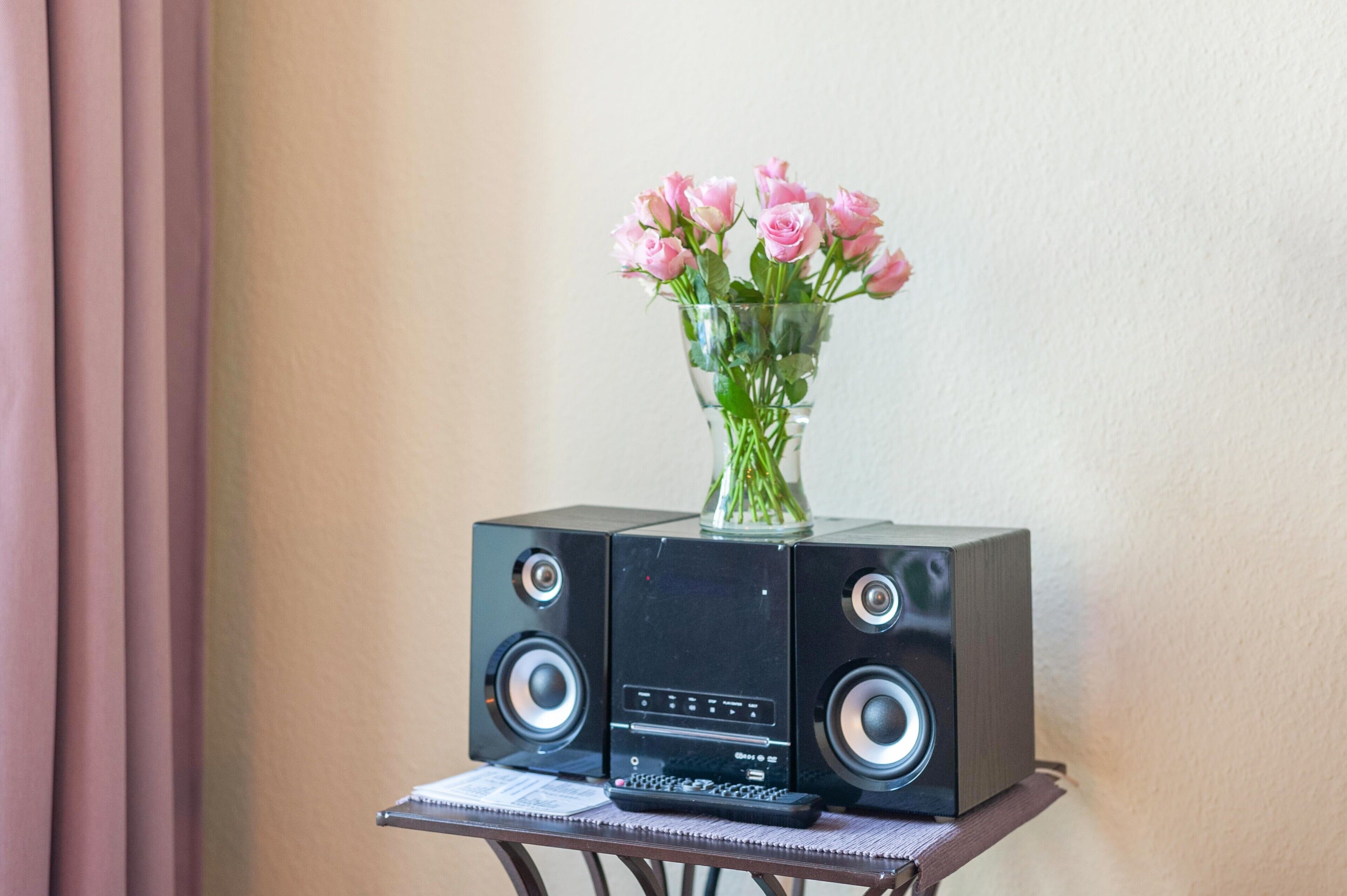 A black speaker system with a vase of pink flowers on top.