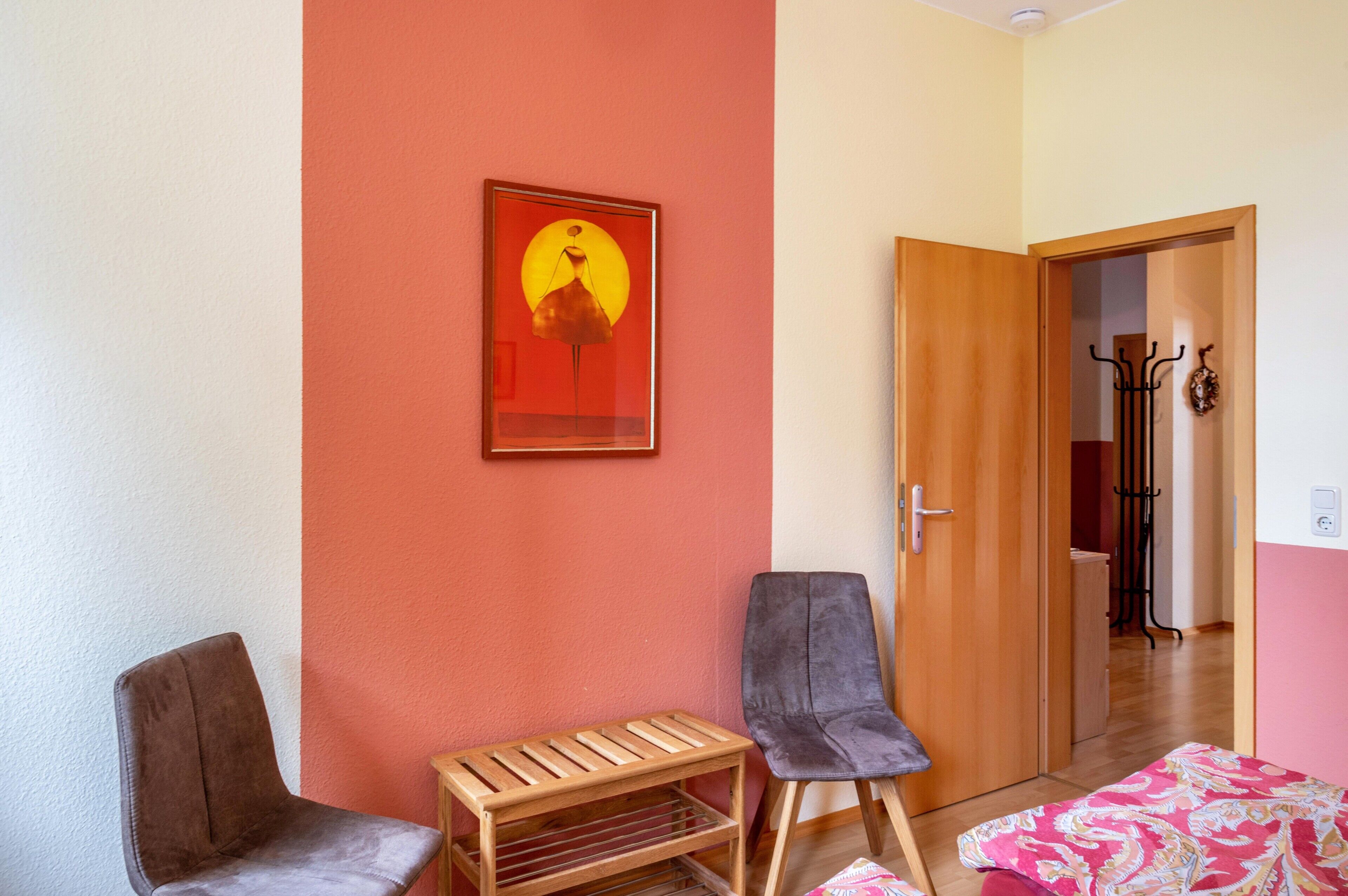 Una habitación con un banco de madera, dos sillas, una puerta que da a otra estancia y un perchero.