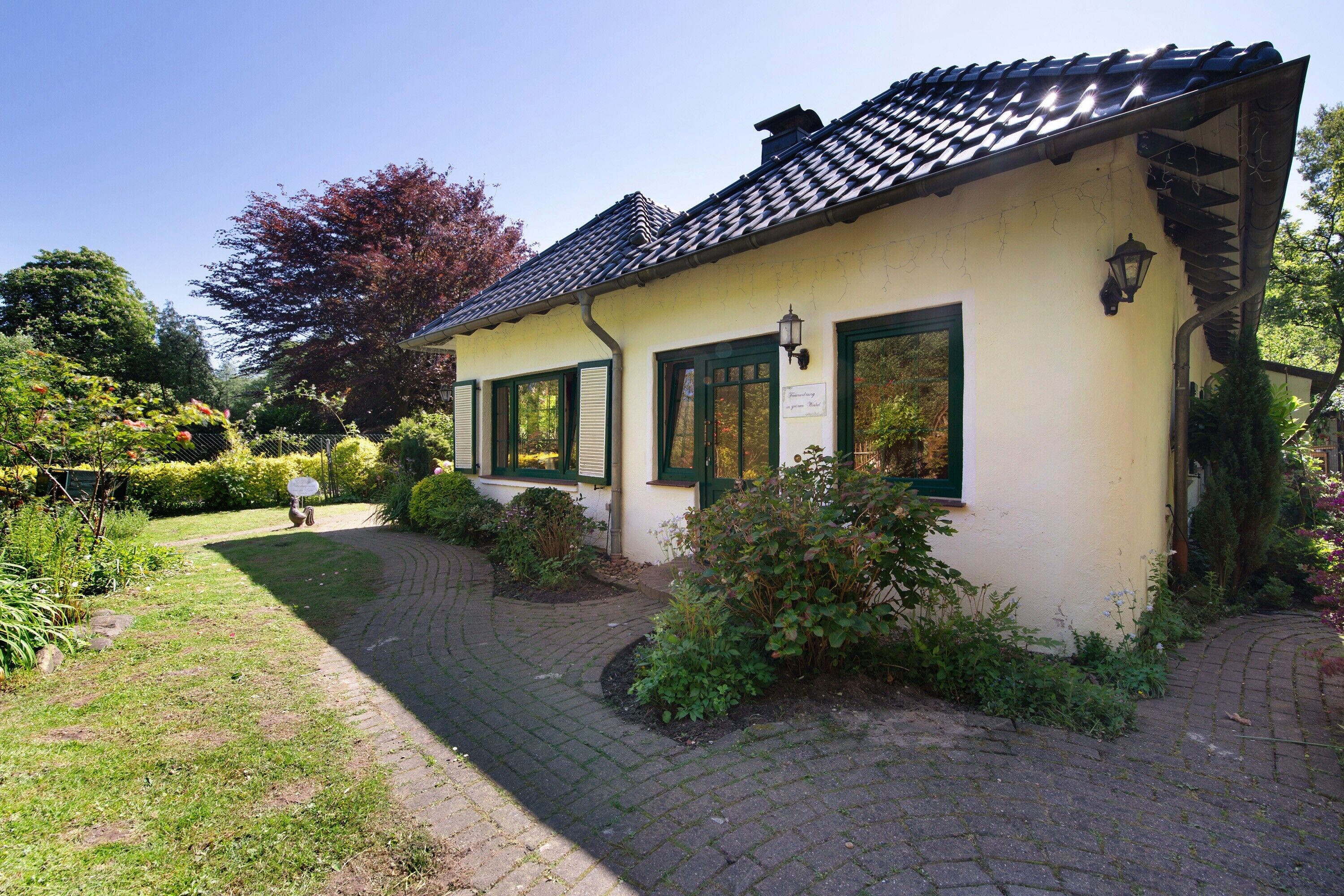 A quaint building with a tiled roof, green shutters, and a paved pathway leading to the entrance.