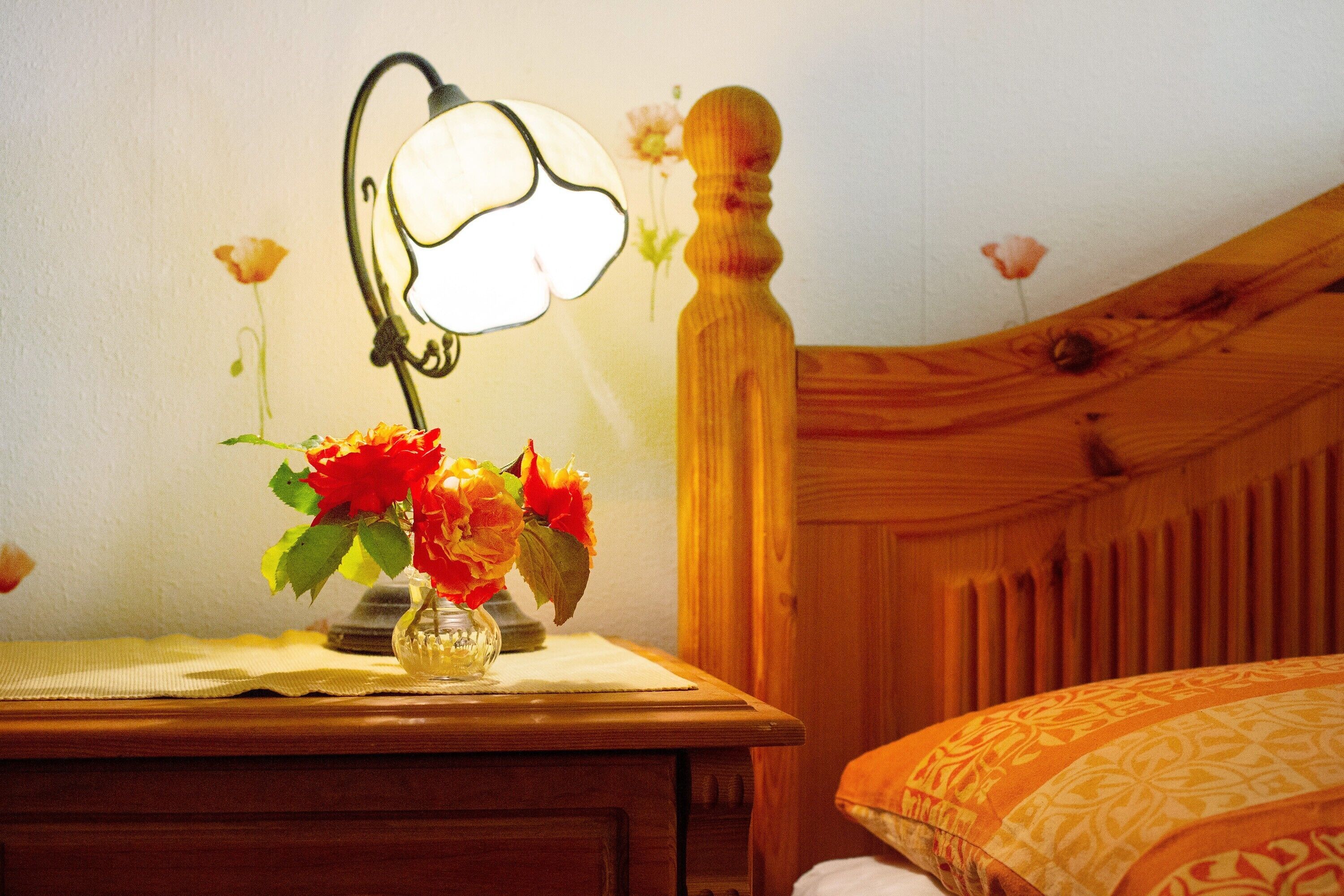 Un comodino in legno con una lampada e un vaso di fiori.
