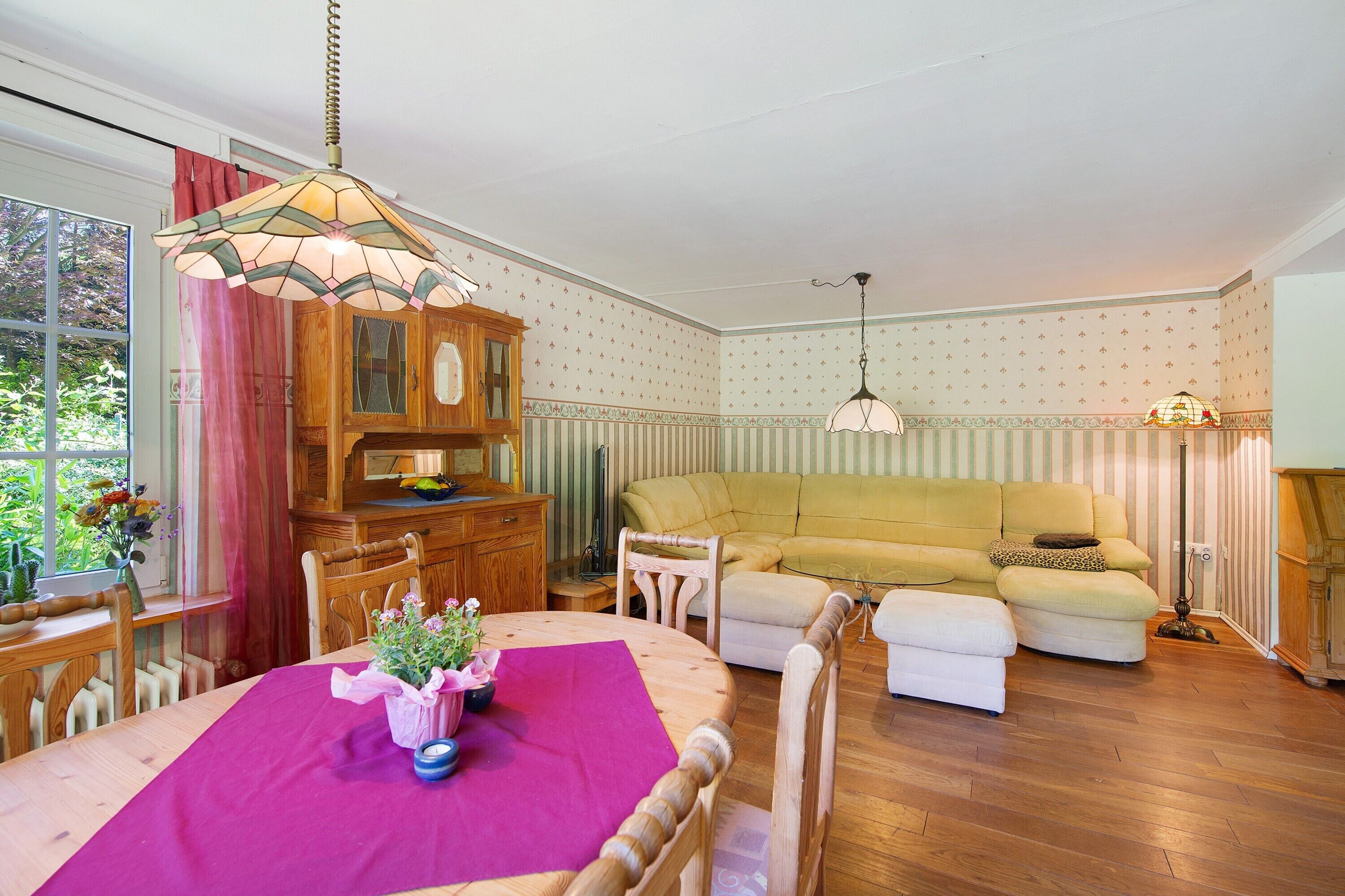 A room with a wooden dining table, a yellow sofa, a wooden cabinet, and a window with curtains.