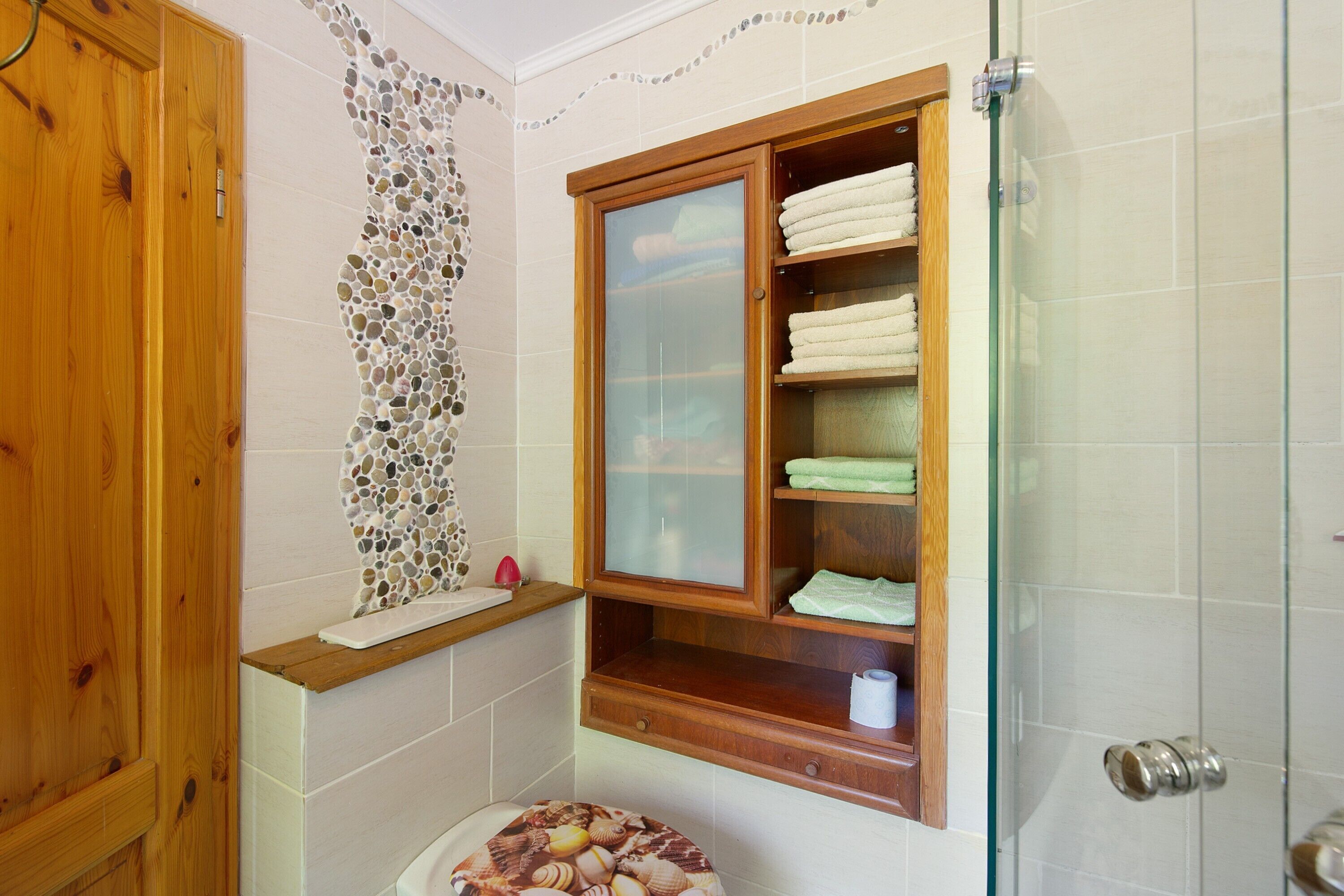 A bathroom with a wooden door, a mosaic wall, a glass shower enclosure, and a wooden shelf with towels.