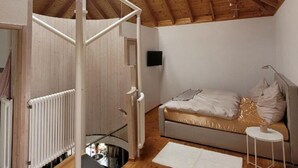 A room with a sloped wooden ceiling, a bed with a white and gold duvet, a small white stool, and a radiator. - Holiday Home 'Lichtdurchflutetes Architektenhaus' with Mountain View, Terrace and Wi-Fi (Balingen)