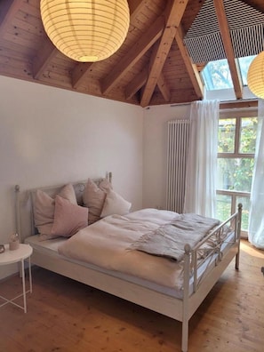 A bedroom with a wooden ceiling, a bed with a metal frame, a bedside table, and a window with curtains. - Holiday Home 'Lichtdurchflutetes Architektenhaus' with Mountain View, Terrace and Wi-Fi (Balingen)
