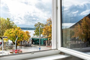 Vista a través de una ventana de una zona junto al lago, con un café, bancos y árboles con follaje otoñal.