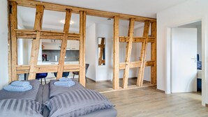 A modern room with exposed wooden beams, a bed with grey bedding, a kitchen area in the background, and a hallway leading to another room. - Apartment '2 Mit Seeblick' with Lake View and Wi-Fi (Überlingen)
