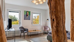 A modern living room with a large window, a wooden floor, a desk with a computer, two chairs, a small table, and a floor lamp. - Apartment '2 Mit Seeblick' with Lake View and Wi-Fi (Überlingen)