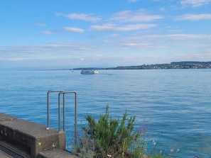 Une vue sur le bord de l’eau, avec un bateau, une rambarde en métal et de la verdure.