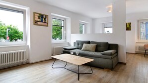 A modern living room with a sofa, a table with two wine glasses, and large windows with blinds. - Apartment '1 Mit Seeblick' with Lake View and Wi-Fi (Überlingen)