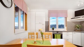 Moderni keittiö, jossa on valkoiset kaapit, ruokapöytä tuoleineen, seinäkello ja ikkuna, josta on näkymä.